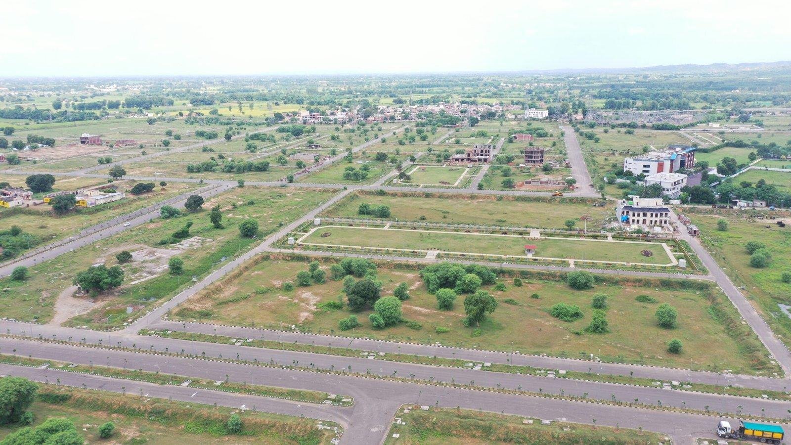 Aerial view of a developing suburban area with grid roads, green fields, and scattered buildings.